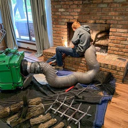 Chimney cleaning equipment including a vacuum, rods and brushes arranged in front of a brick fireplace