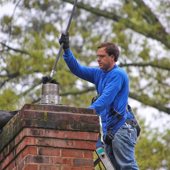 Sweep on a ladder pushing a brush rod into a stainless steel flue on top of a brick chimney
