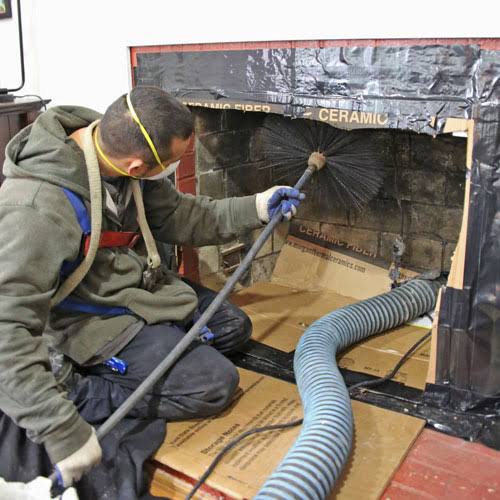 Technician with a respirator pushing a rotary chimney brush up into a fireplace sealed with protective sheeting