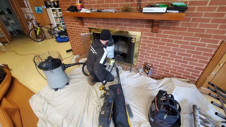 Technician working on a brass-framed fireplace in a brick wall with drop cloths covering the floor