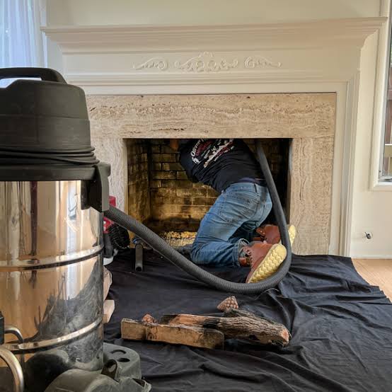 Technician leaning into a fireplace beneath a white carved mantel with a vacuum hose running into the firebox