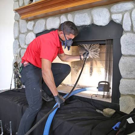 Technician in a red shirt and respirator cleaning a fireplace framed in large stone
